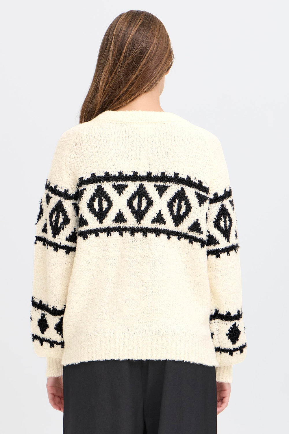 Person wearing a cream sweater with black pattern on a white background