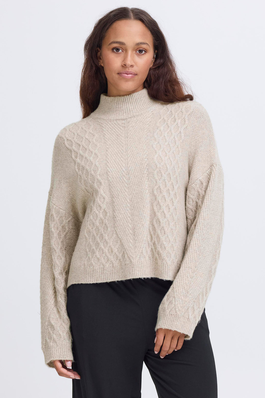 Woman wearing a beige cable knit sweater against a white background