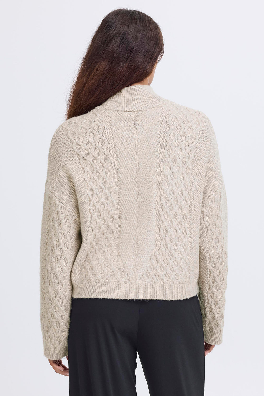 Person wearing a beige cable knit sweater on a white background