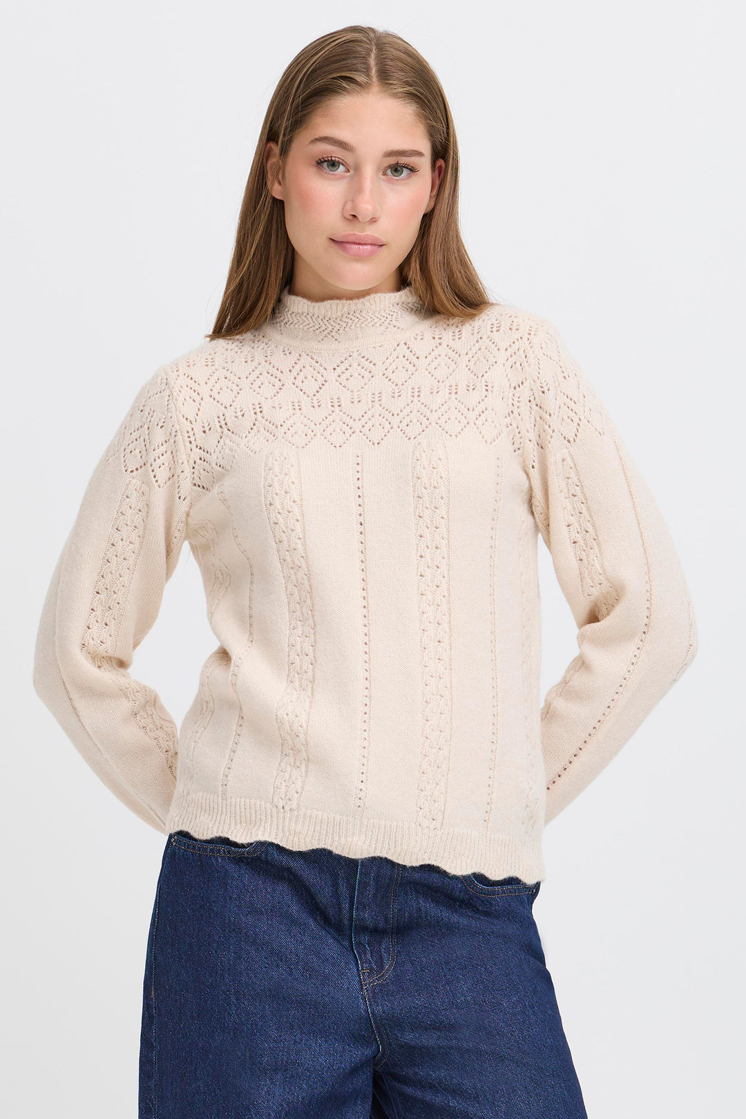 Woman wearing a beige knitted sweater and blue jeans on a white background