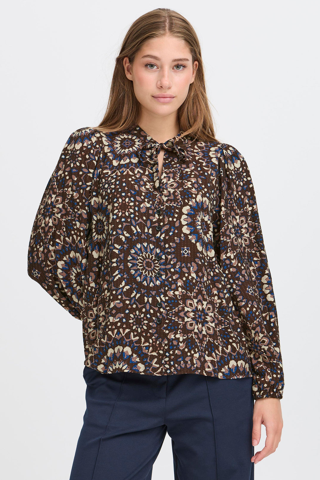 Woman wearing a patterned blouse and dark pants on a white background