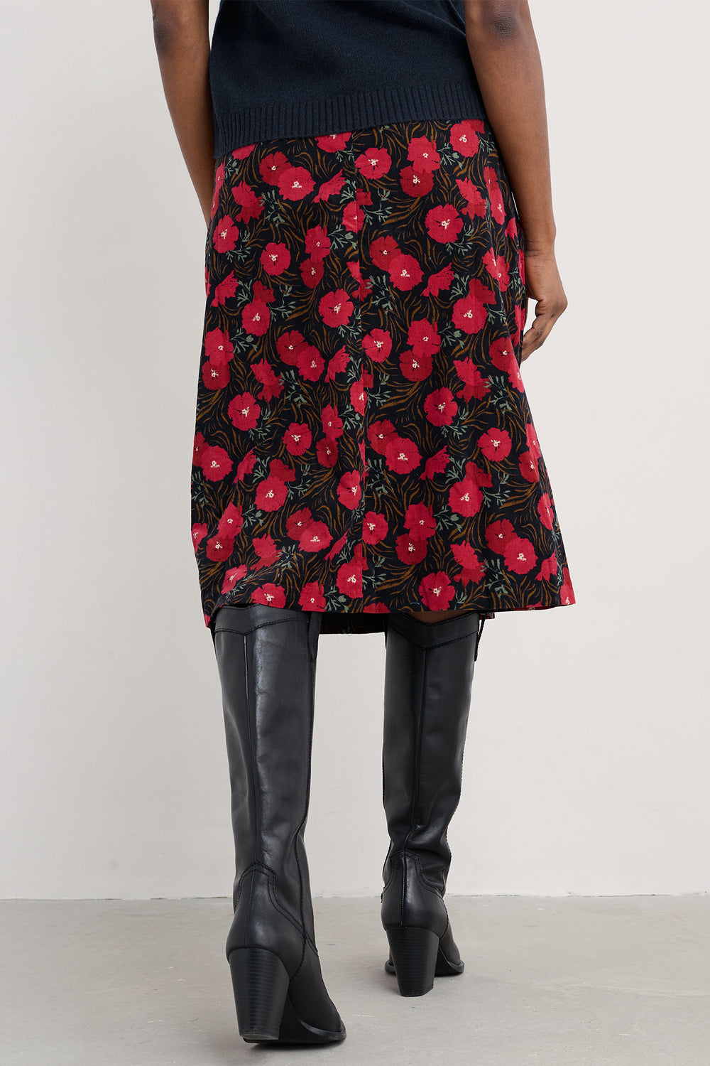 Person wearing a black skirt with red floral pattern and black knee-high boots on a white background