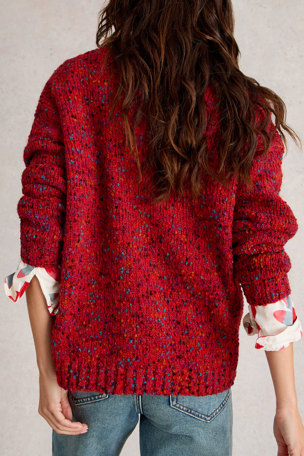 Person wearing a red textured sweater with rolled-up sleeves on a neutral background