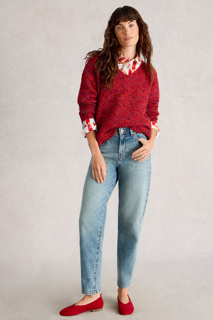 Woman wearing a red sweater, light blue jeans, and red shoes on a plain background