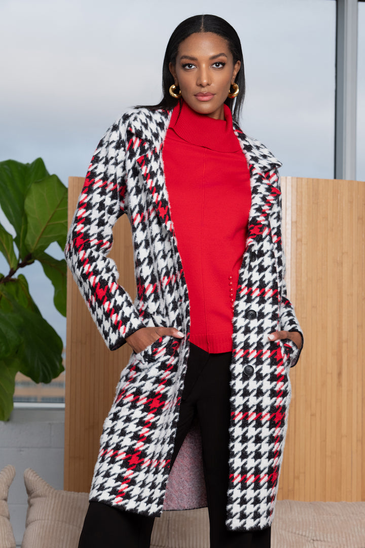 Woman wearing a houndstooth patterned coat over a red top, standing indoors.