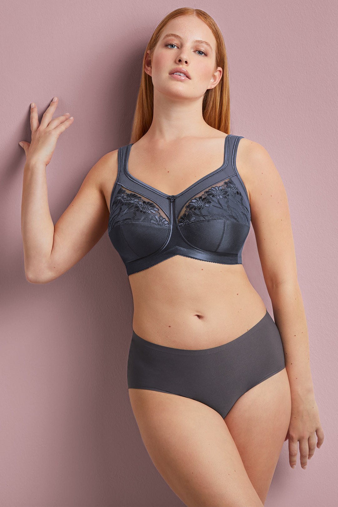 Woman wearing a dark gray bra and underwear set against a pink background