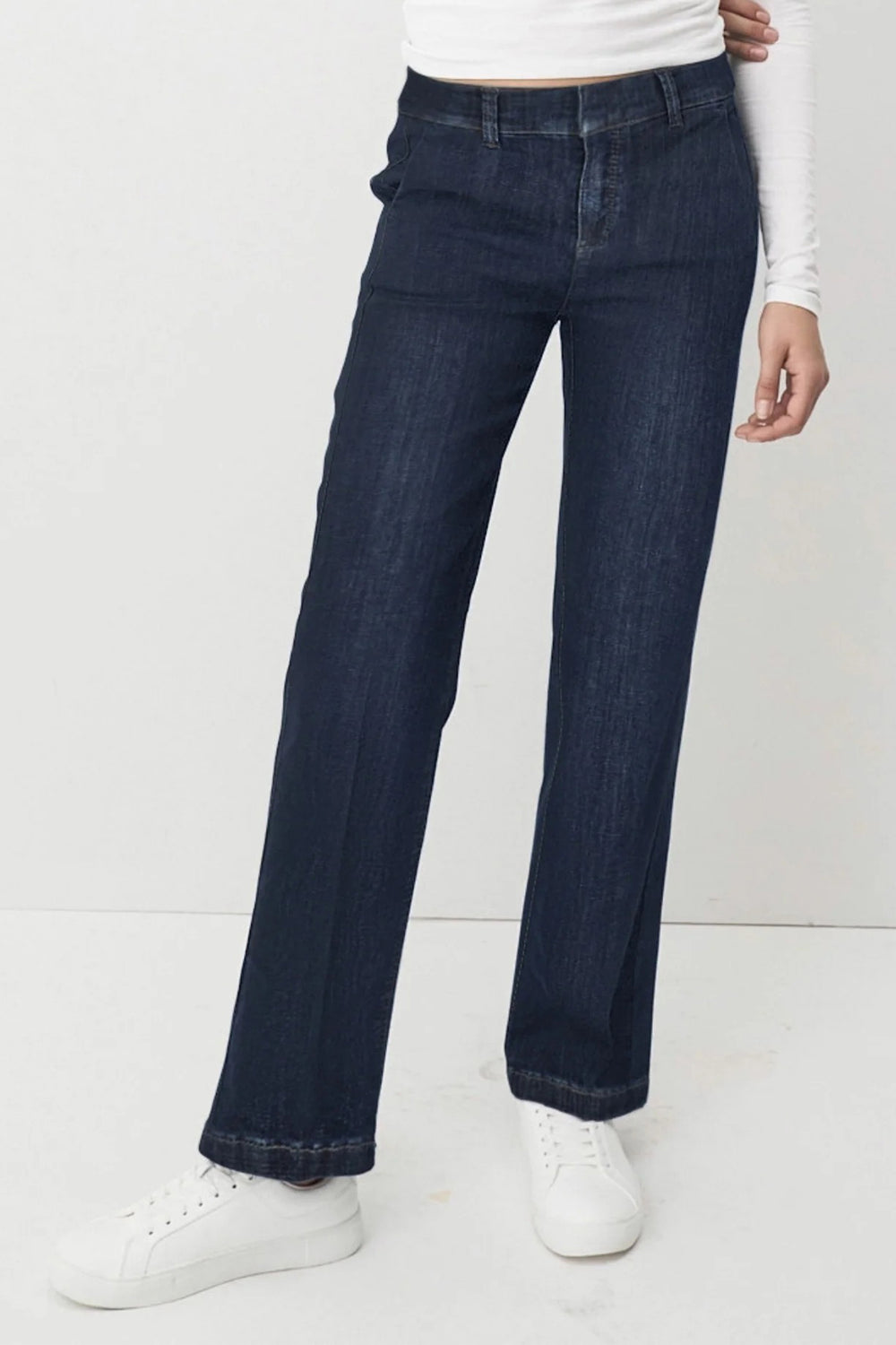 Person wearing dark blue jeans and white sneakers on a plain background