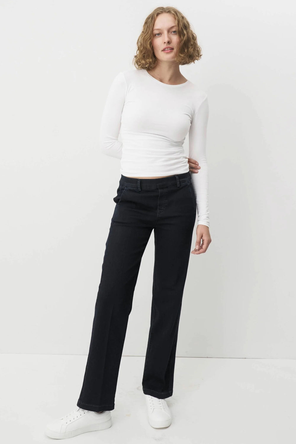 Woman wearing a white long-sleeve top and navy pants on a white background