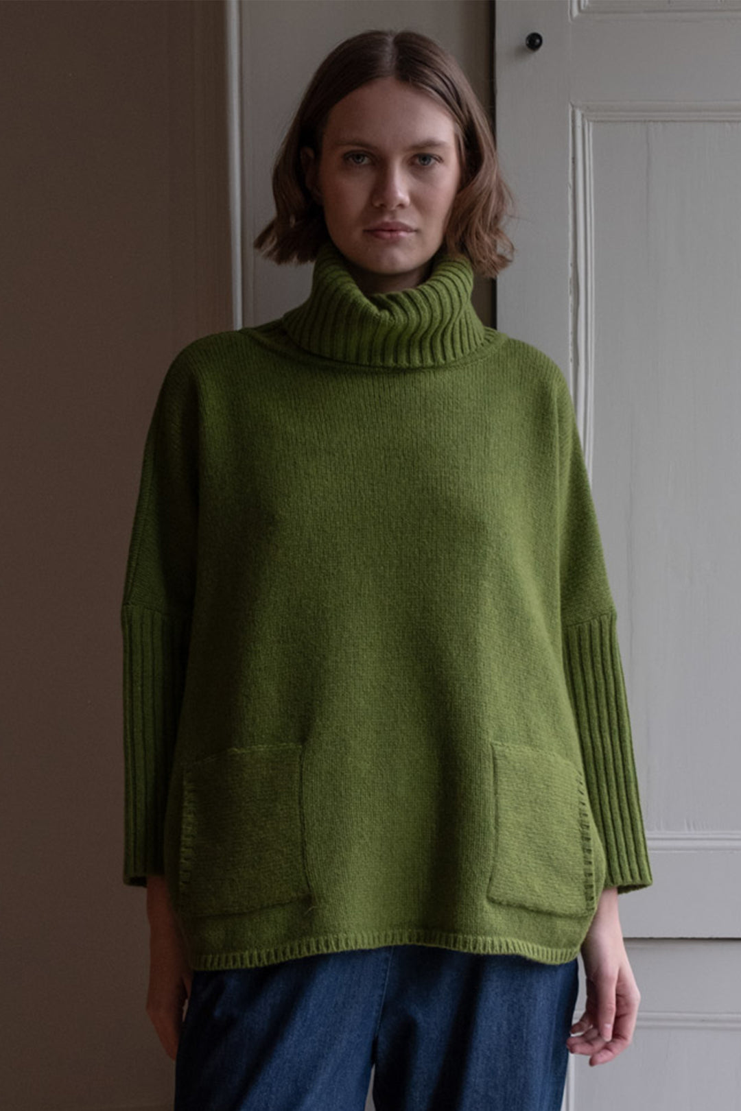 Woman wearing a green sweater standing against a plain background
