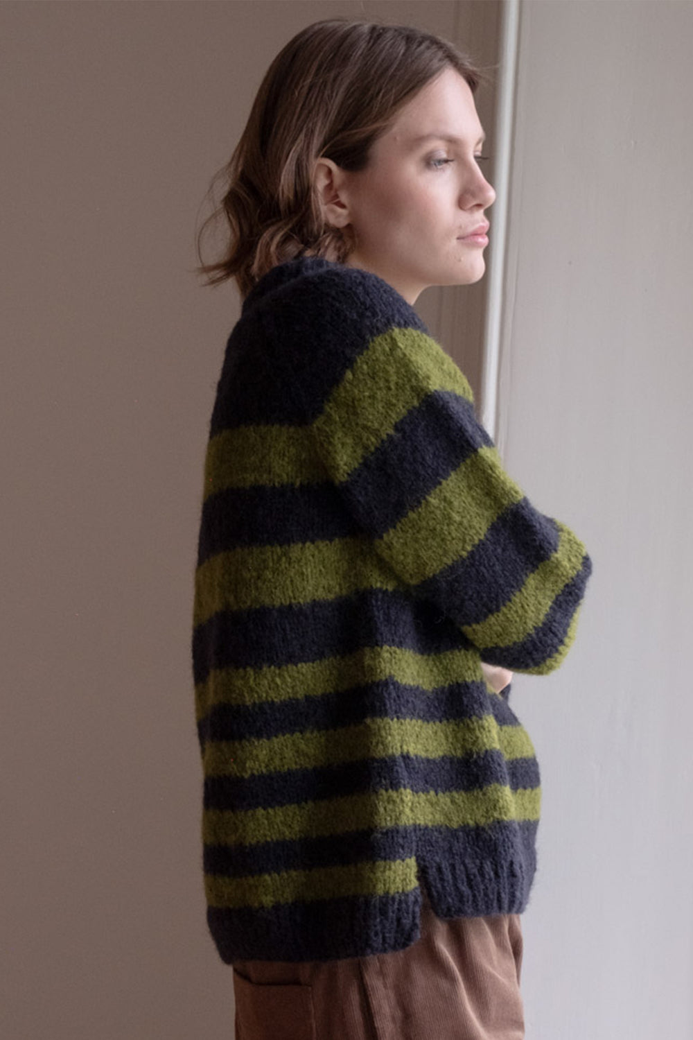 Woman wearing a green and navy striped sweater against a plain background
