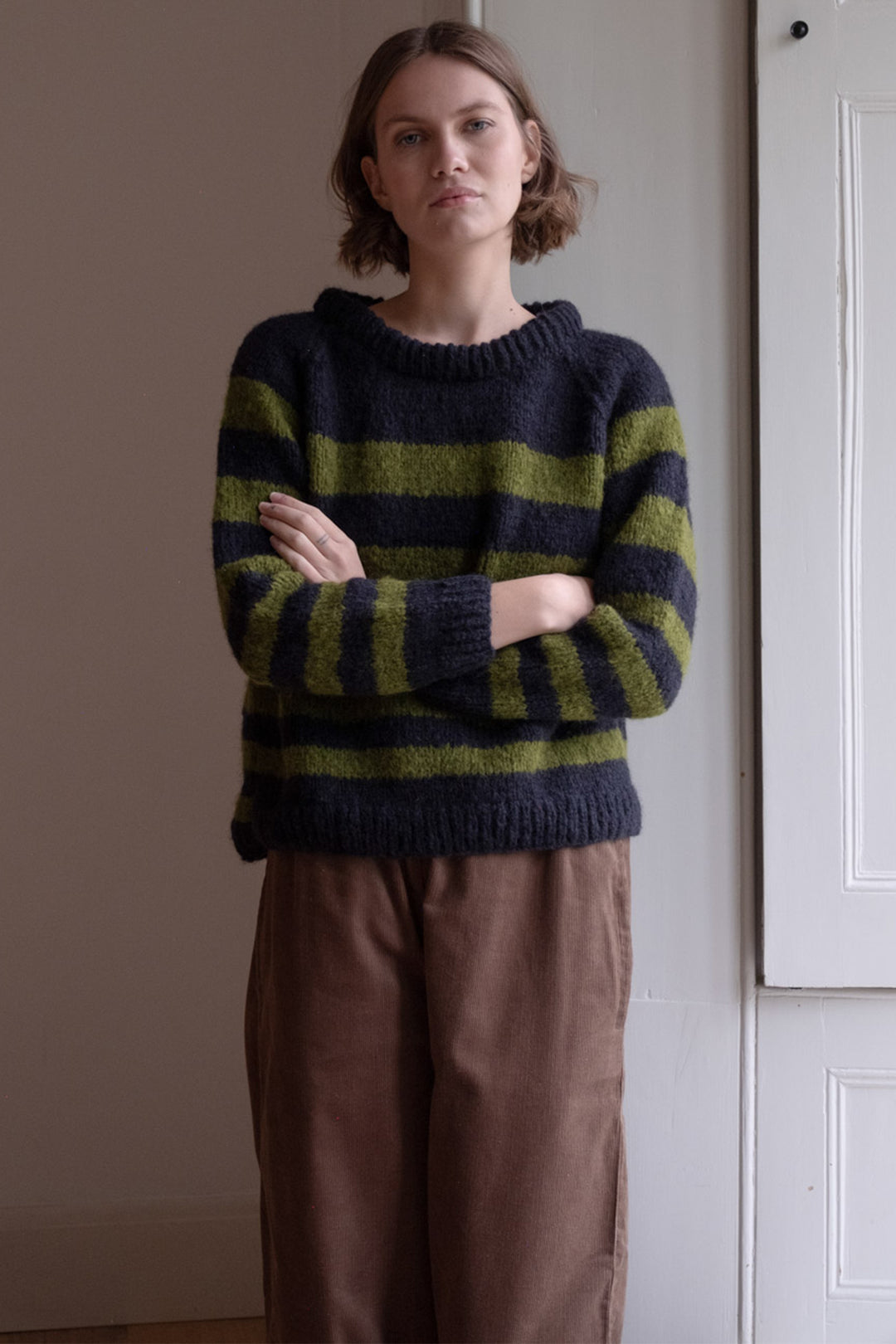 Person wearing a striped sweater standing against a plain wall.