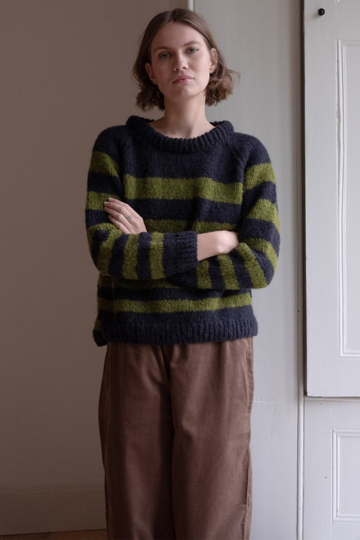 Person wearing a striped sweater standing against a plain wall.