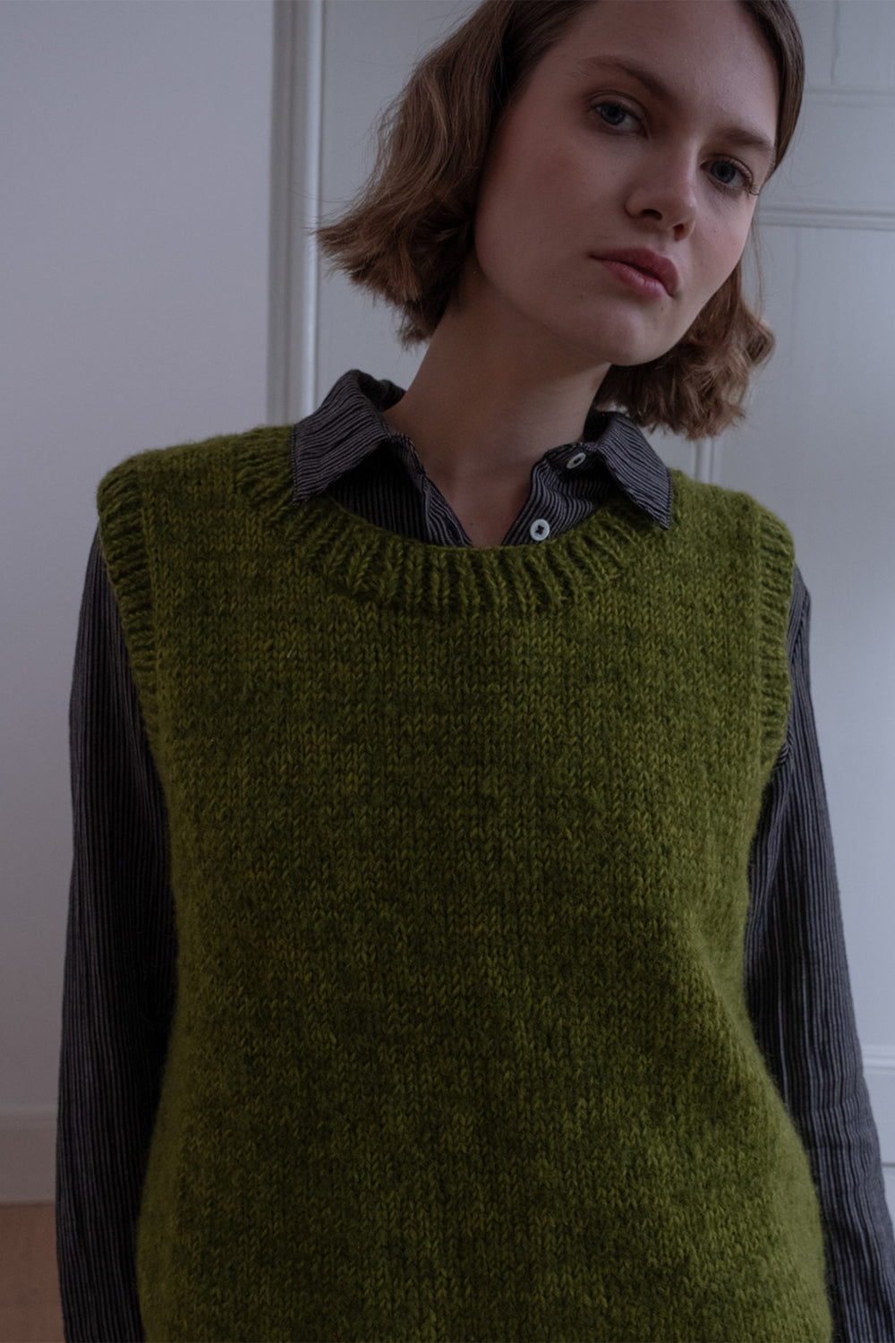 Person wearing a green knitted vest over a dark shirt against a plain background