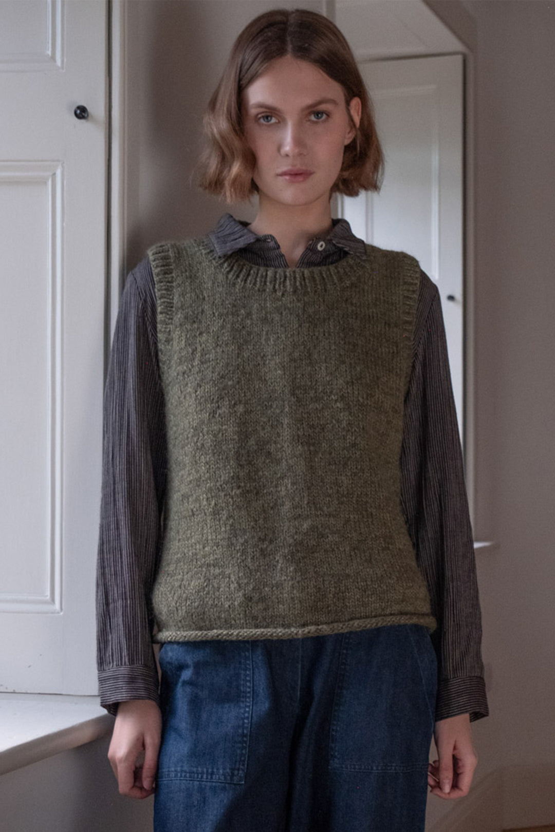 Person wearing a green knitted vest over a collared shirt in an indoor setting