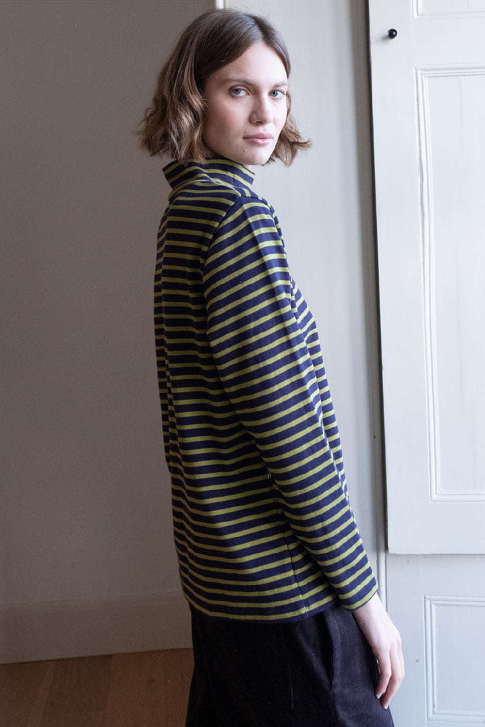 Woman wearing a striped shirt standing against a plain wall.
