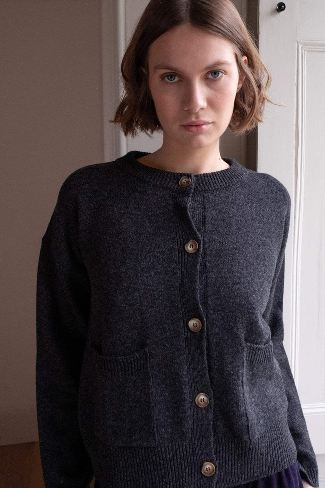 Woman wearing a dark gray cardigan with button details against a neutral background