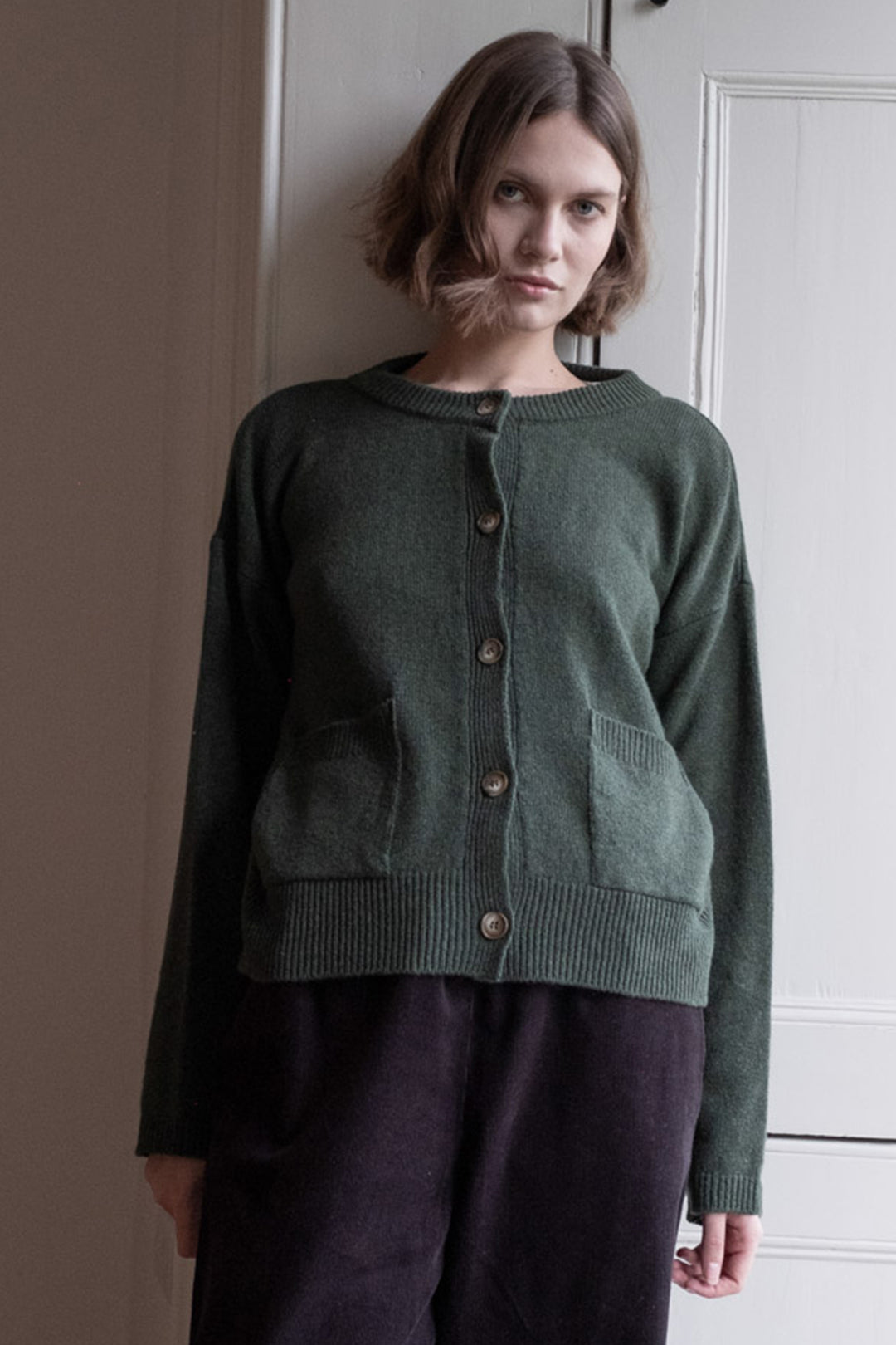 Woman wearing a green cardigan standing against a neutral wall.
