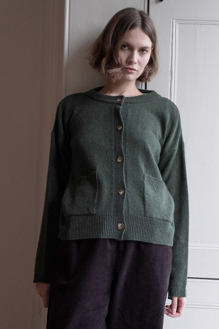 Woman wearing a green cardigan standing against a neutral wall.