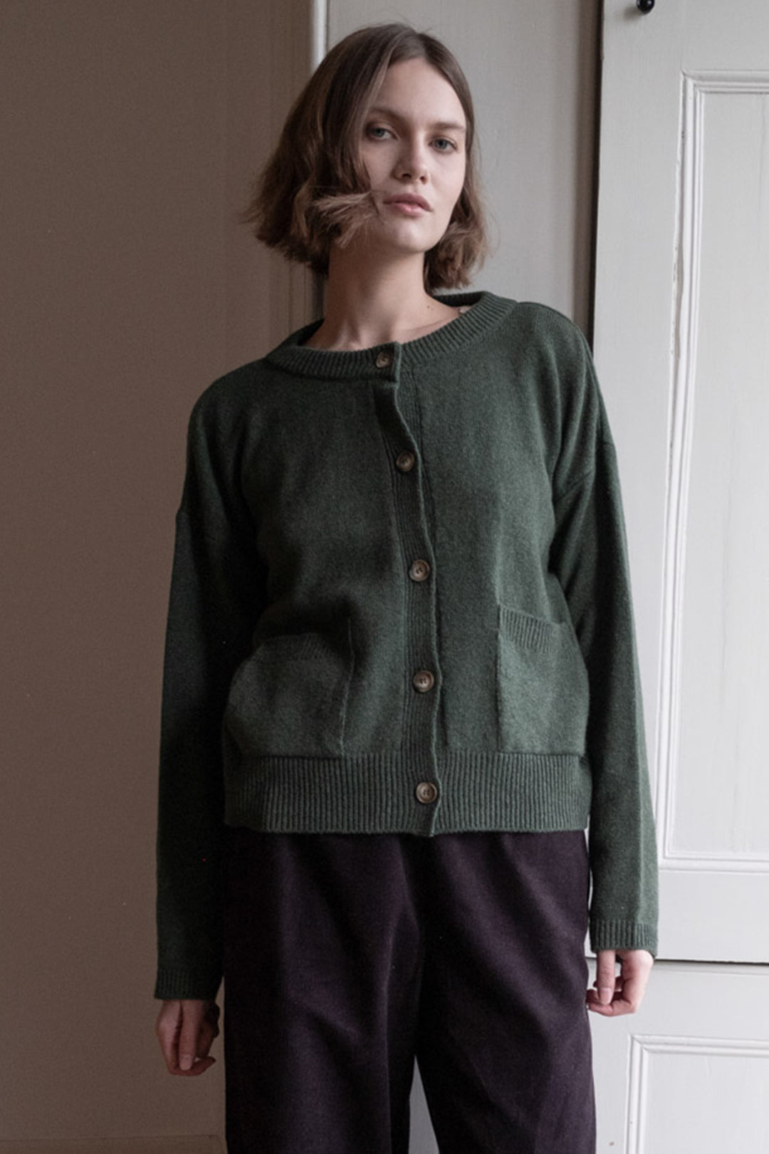 Person wearing a green cardigan and dark pants against a neutral background