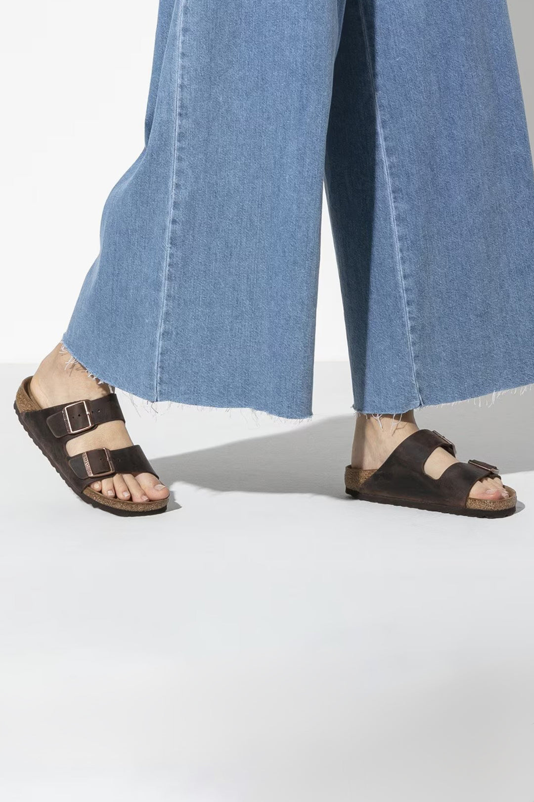 Person wearing black sandals and blue jeans on a white background