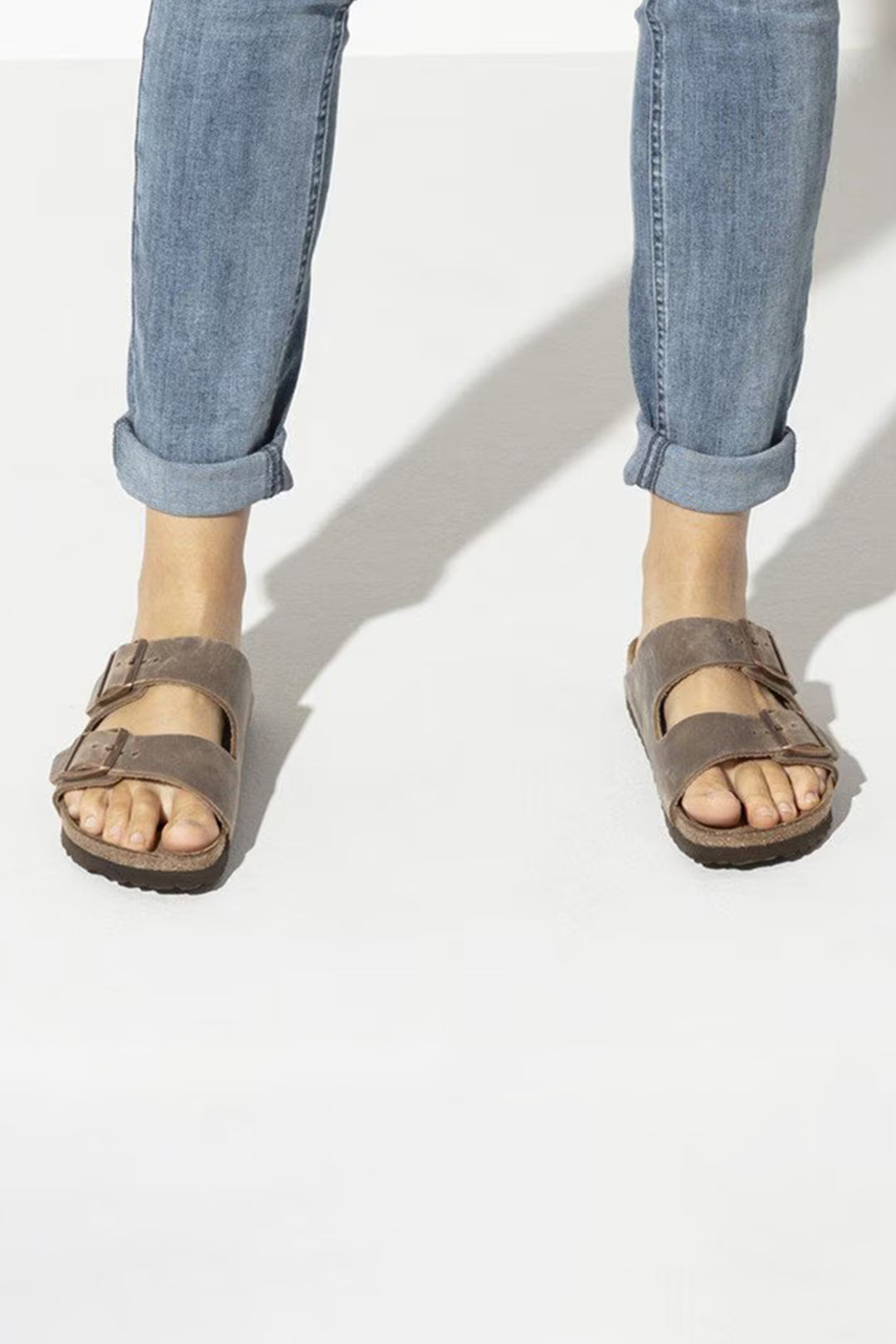 Person wearing brown sandals and light blue jeans on a white background