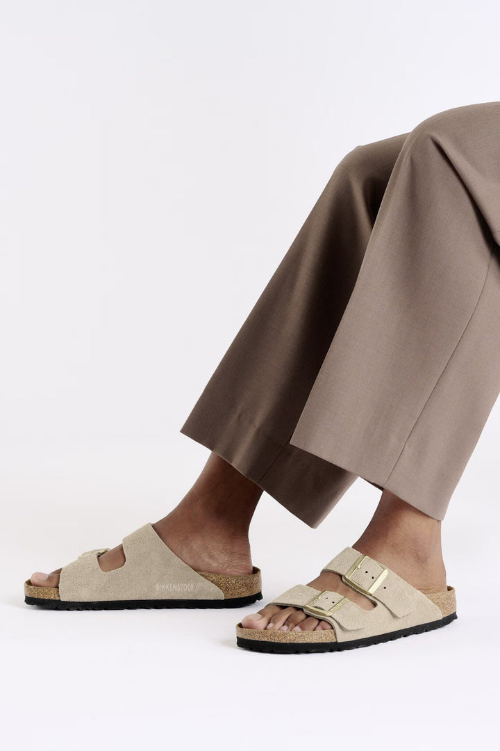 Person wearing beige sandals and brown pants on a white background