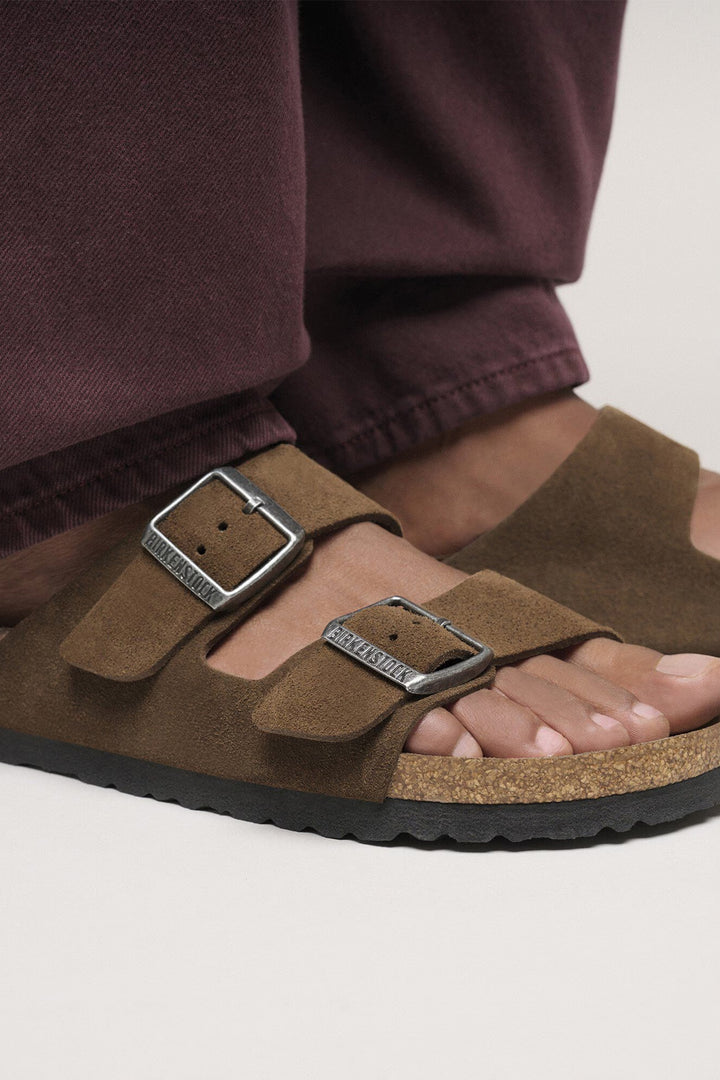 Brown sandals with buckles worn by a person in maroon pants on a light background