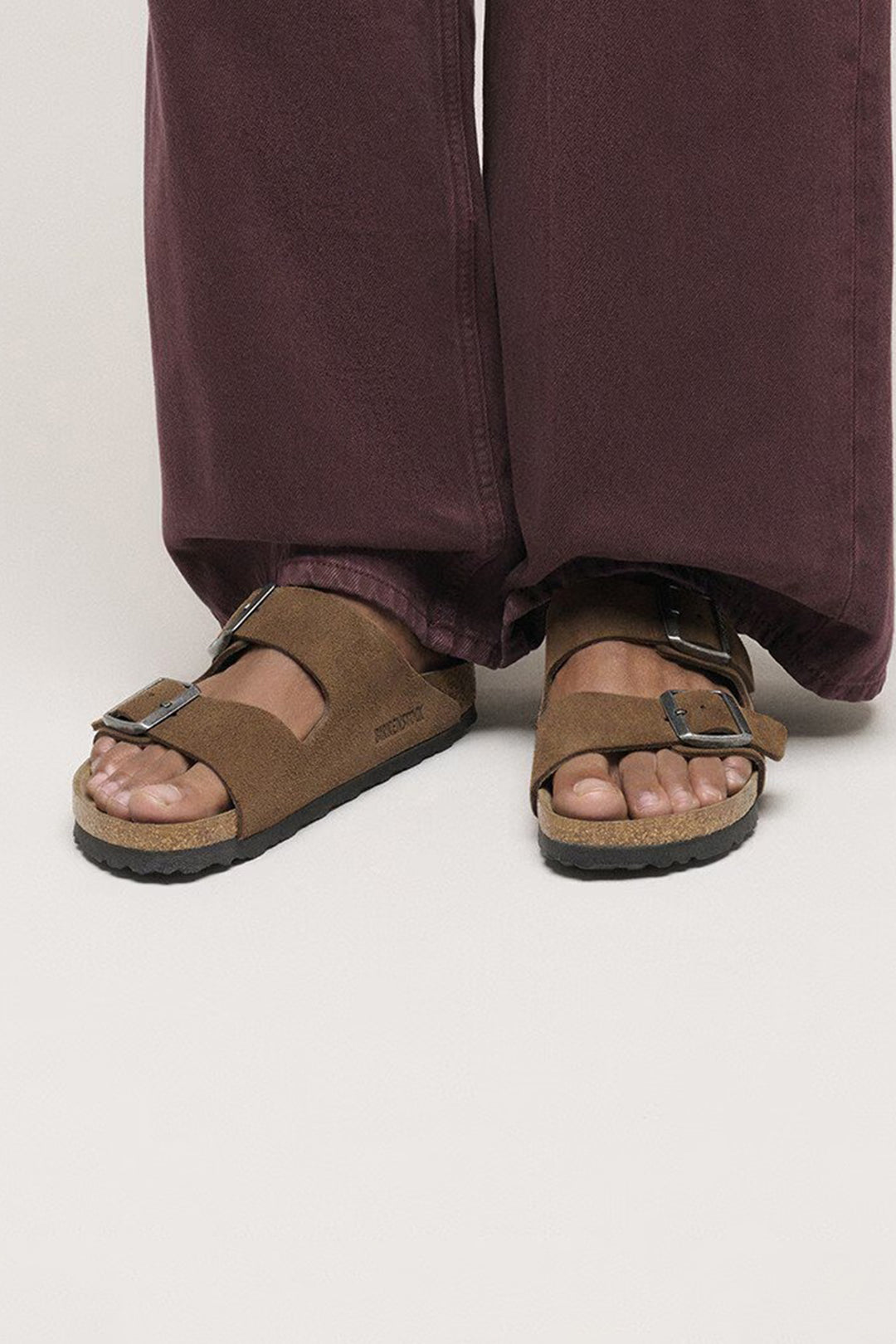 Brown sandals worn with wide-leg pants on a plain background