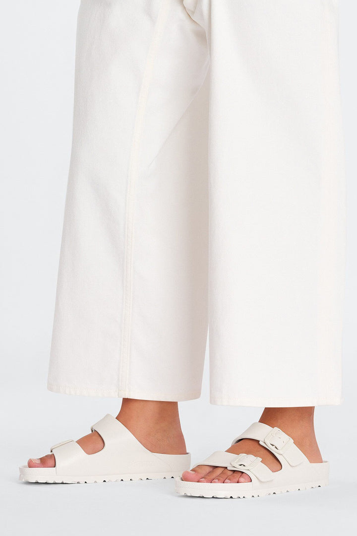White sandals worn with white pants on a light gray background