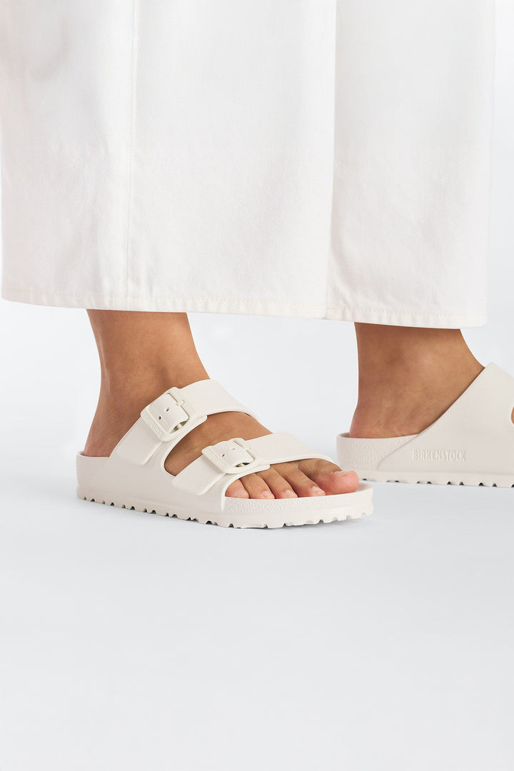 White sandals worn with white pants on a light gray background
