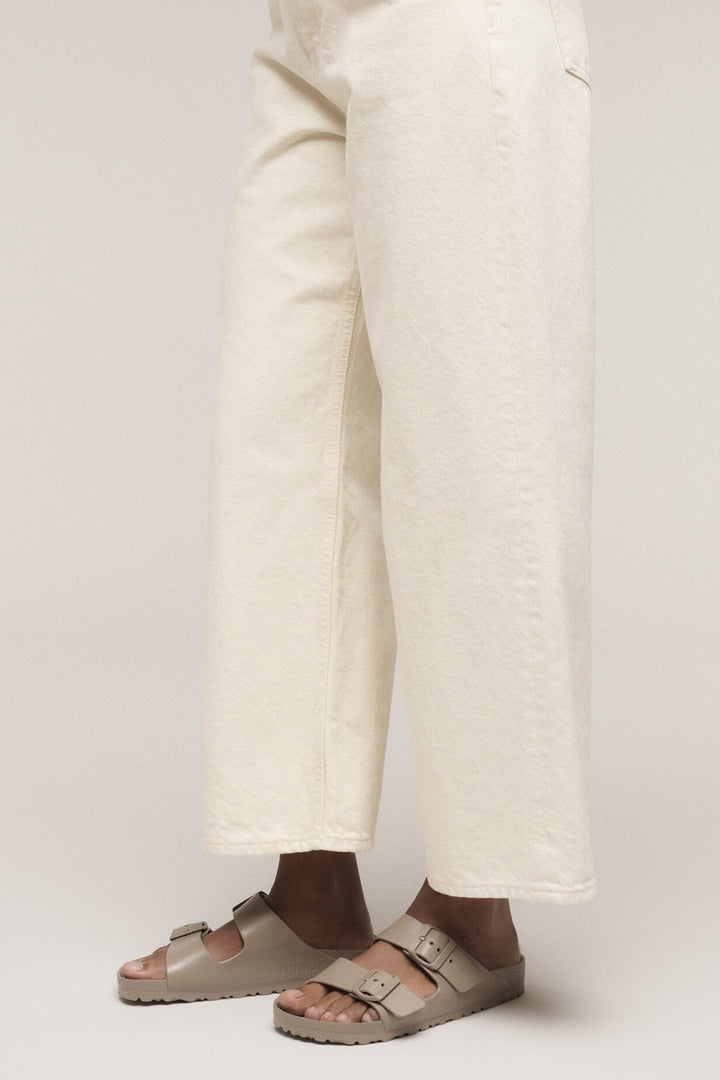 Person wearing white pants and beige sandals on a plain background