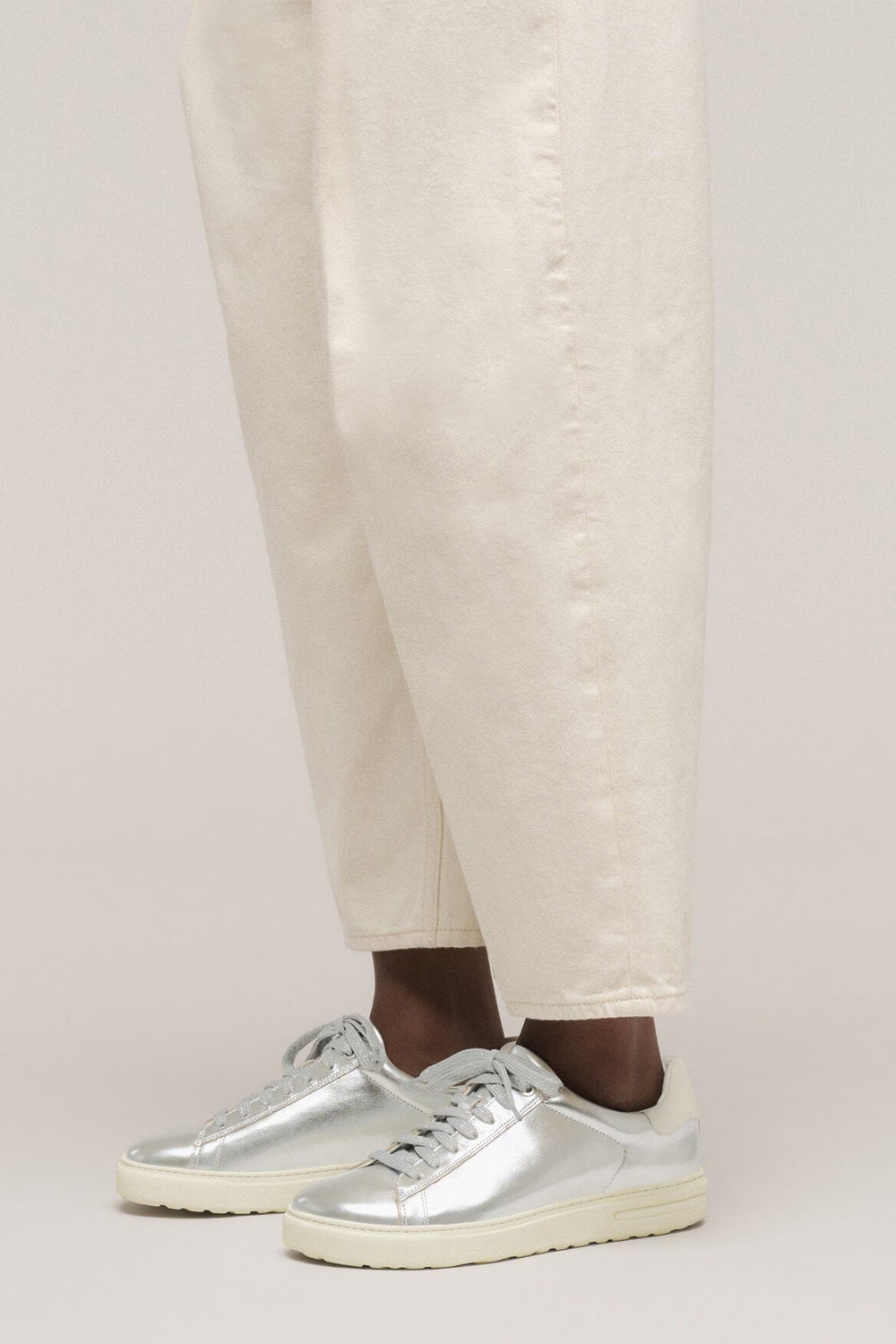 Person wearing silver sneakers and light-colored pants on a plain background