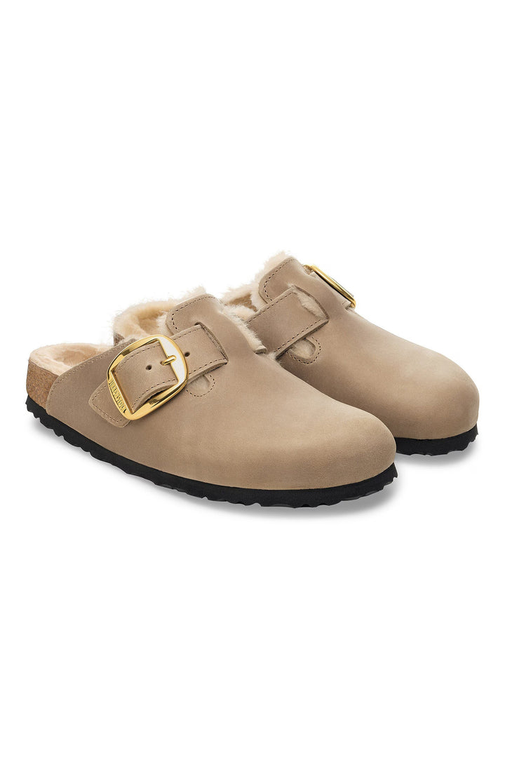 Pair of beige clogs with gold buckles on a white background