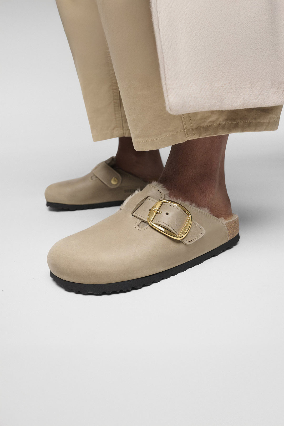 Beige clogs with gold buckle on a neutral background