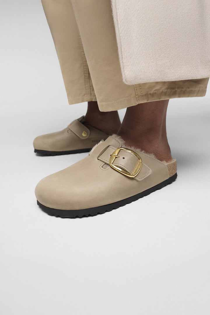 Beige clogs with gold buckle on a neutral background