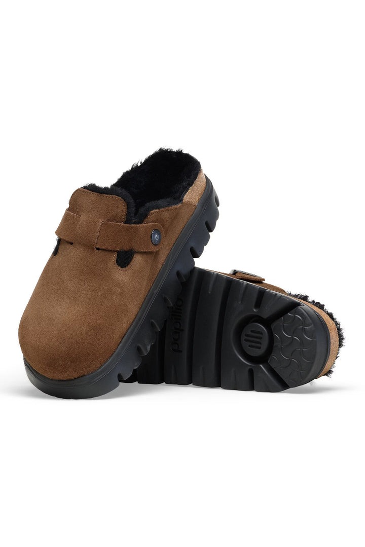Brown suede clogs with black soles on a white background
