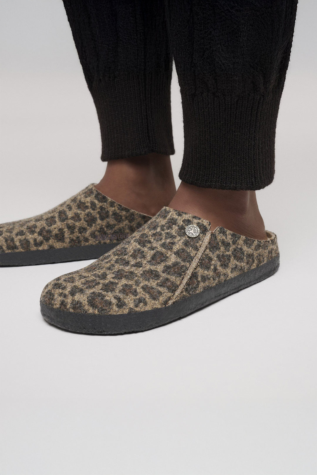 Leopard print slippers worn with black pants on a white background