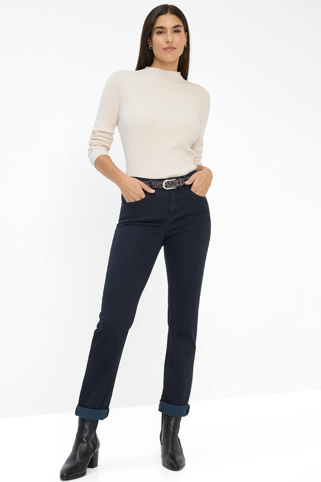 Woman wearing a cream sweater, navy pants, and black boots on a white background