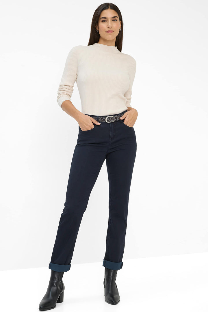 Woman wearing a cream sweater, navy pants, and black boots on a white background