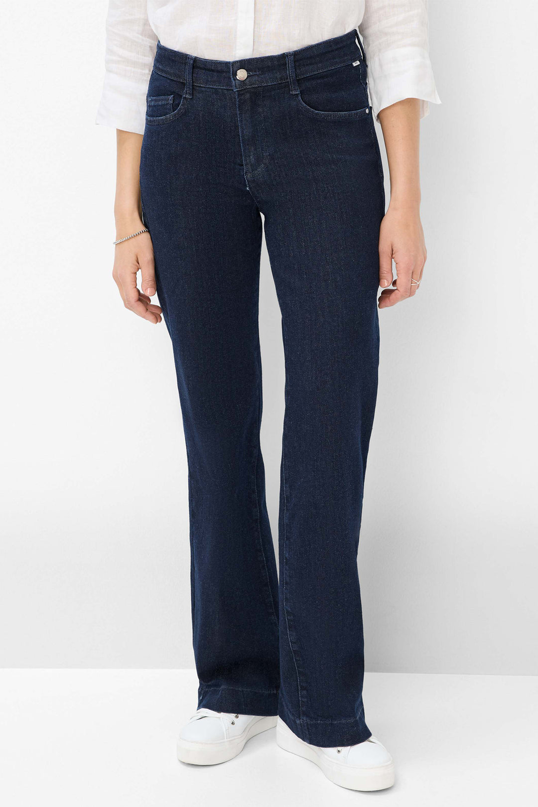 Person wearing dark blue jeans and white shoes on a plain background
