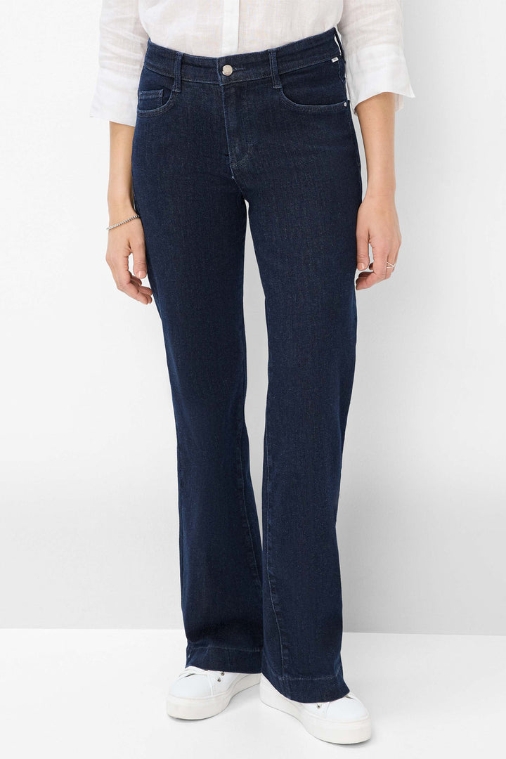 Person wearing dark blue jeans and white shoes on a plain background