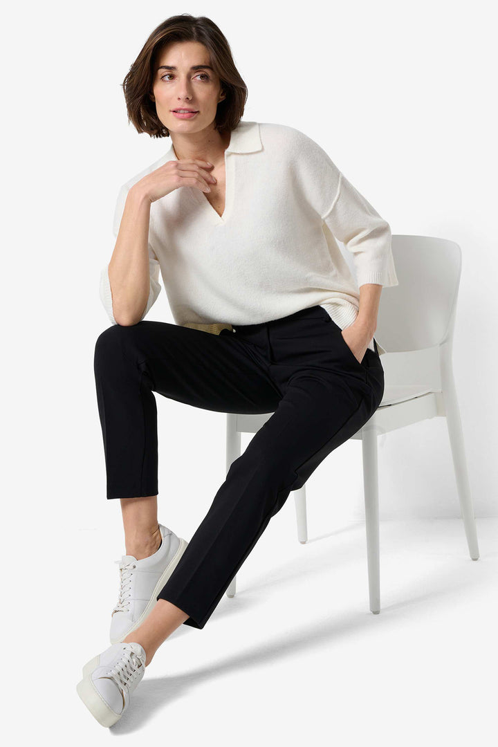Woman sitting on a white chair wearing a white blouse and black pants.