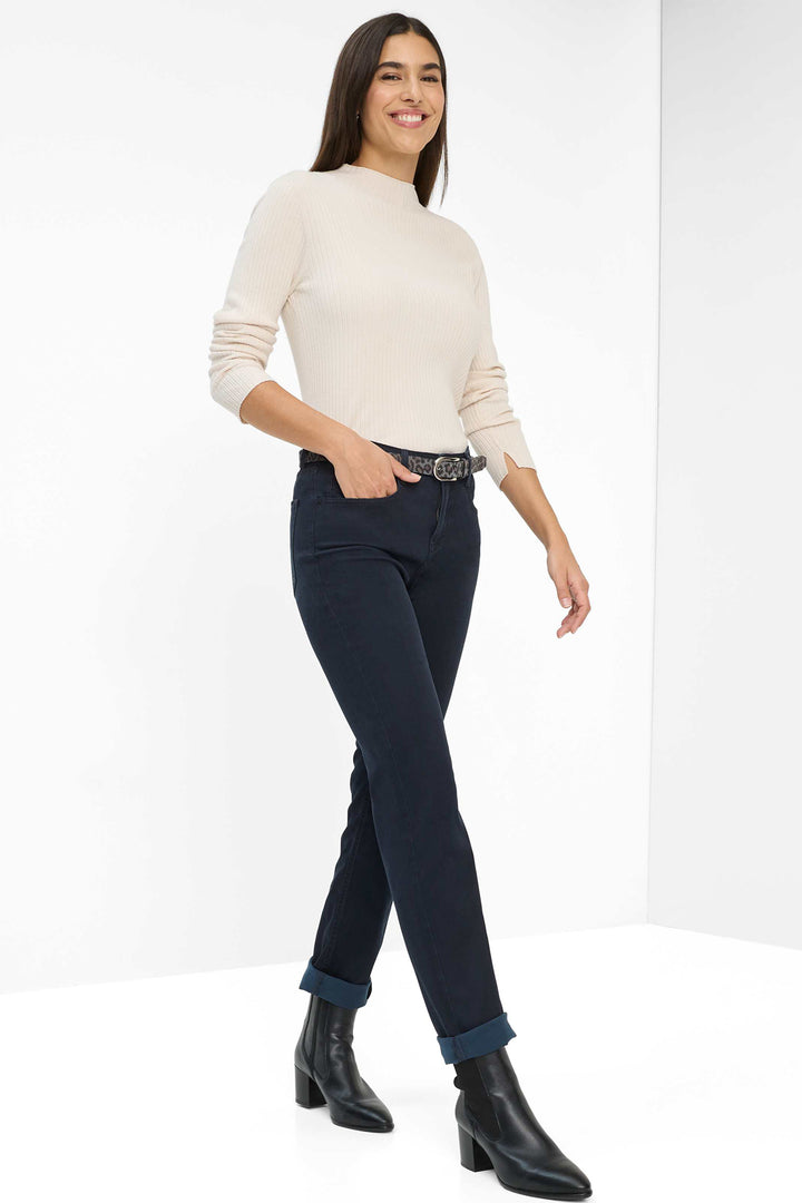 Woman wearing a cream sweater and dark jeans with black boots on a white background