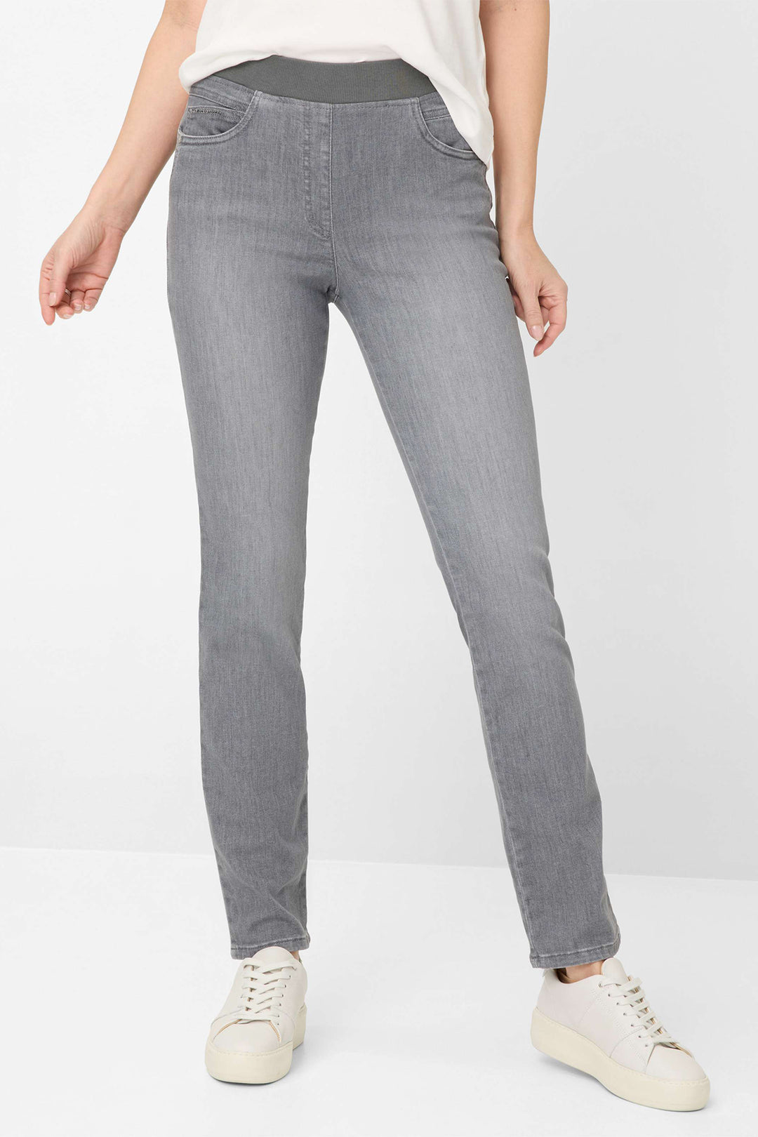 Person wearing gray jeans and white sneakers on a white background