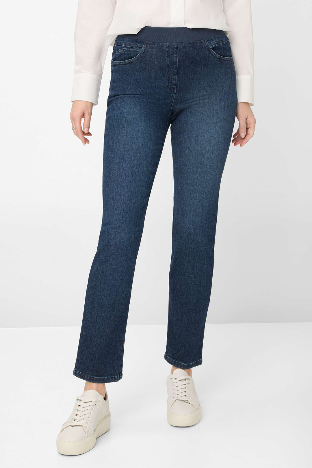 Person wearing dark blue jeans and white sneakers on a white background