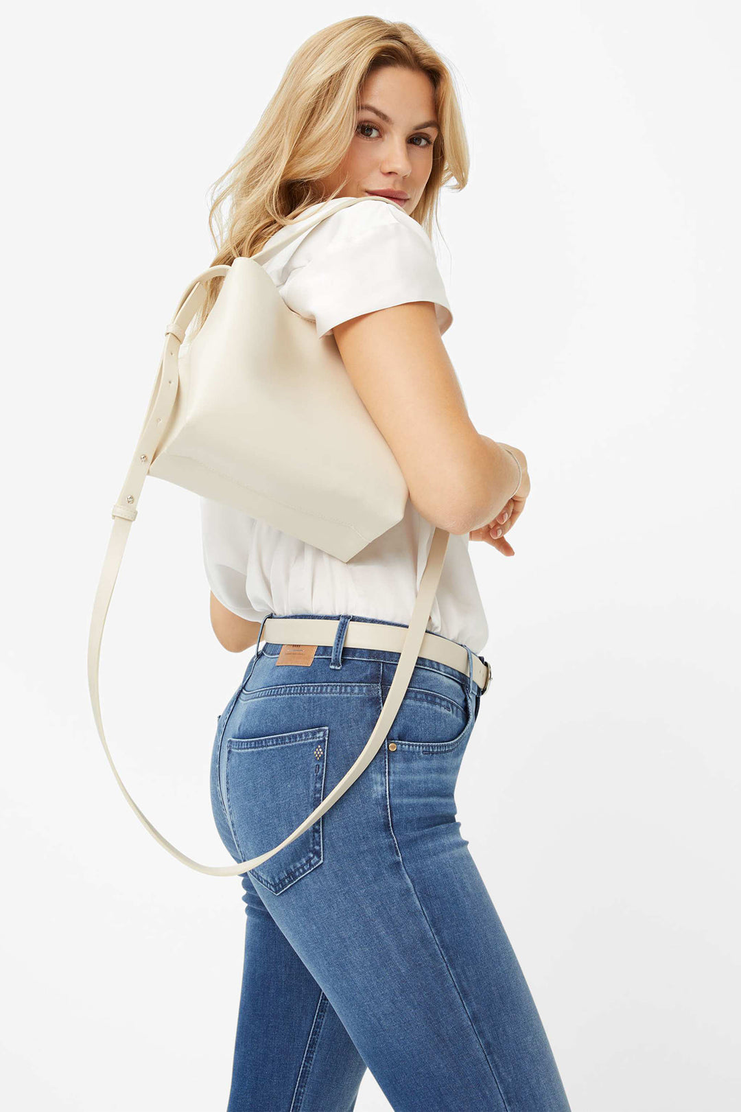 Woman wearing a white t-shirt and blue jeans with a beige backpack on a white background