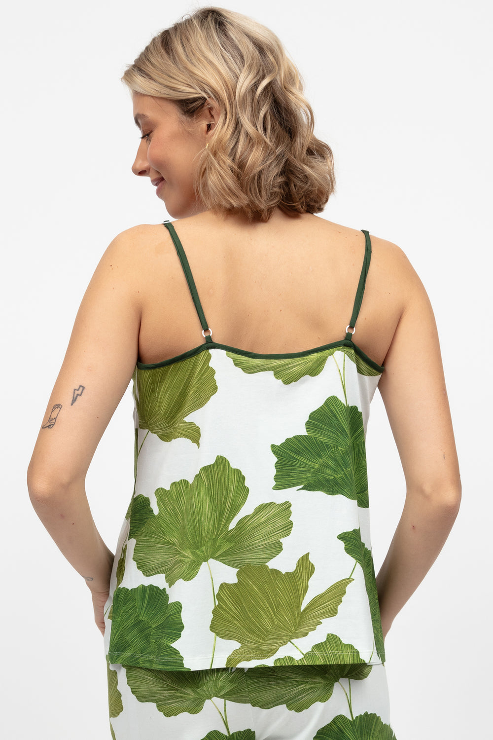Woman wearing a sleeveless top with green leaf pattern on a white background