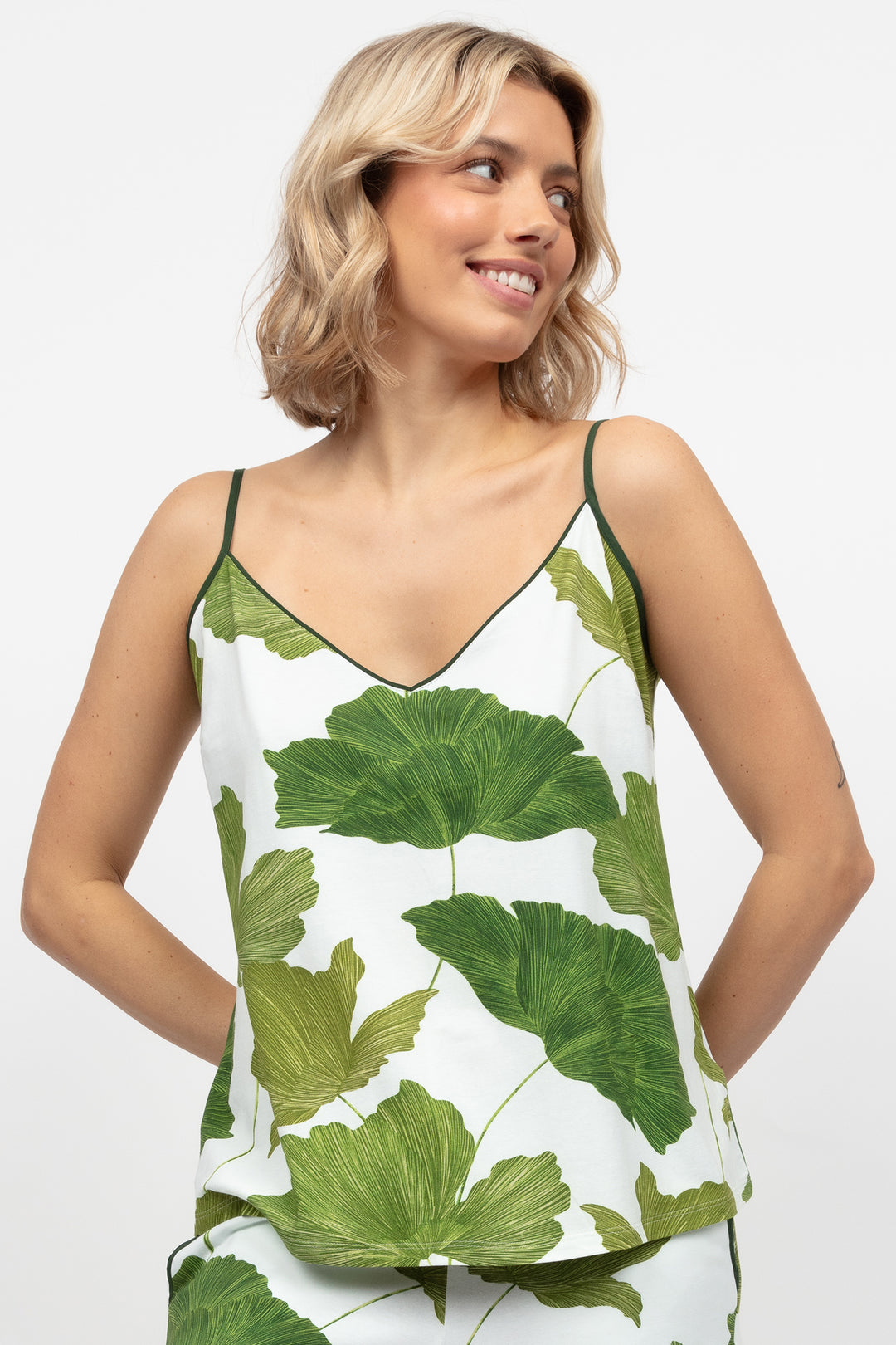Woman wearing a sleeveless top with green leaf pattern on a white background