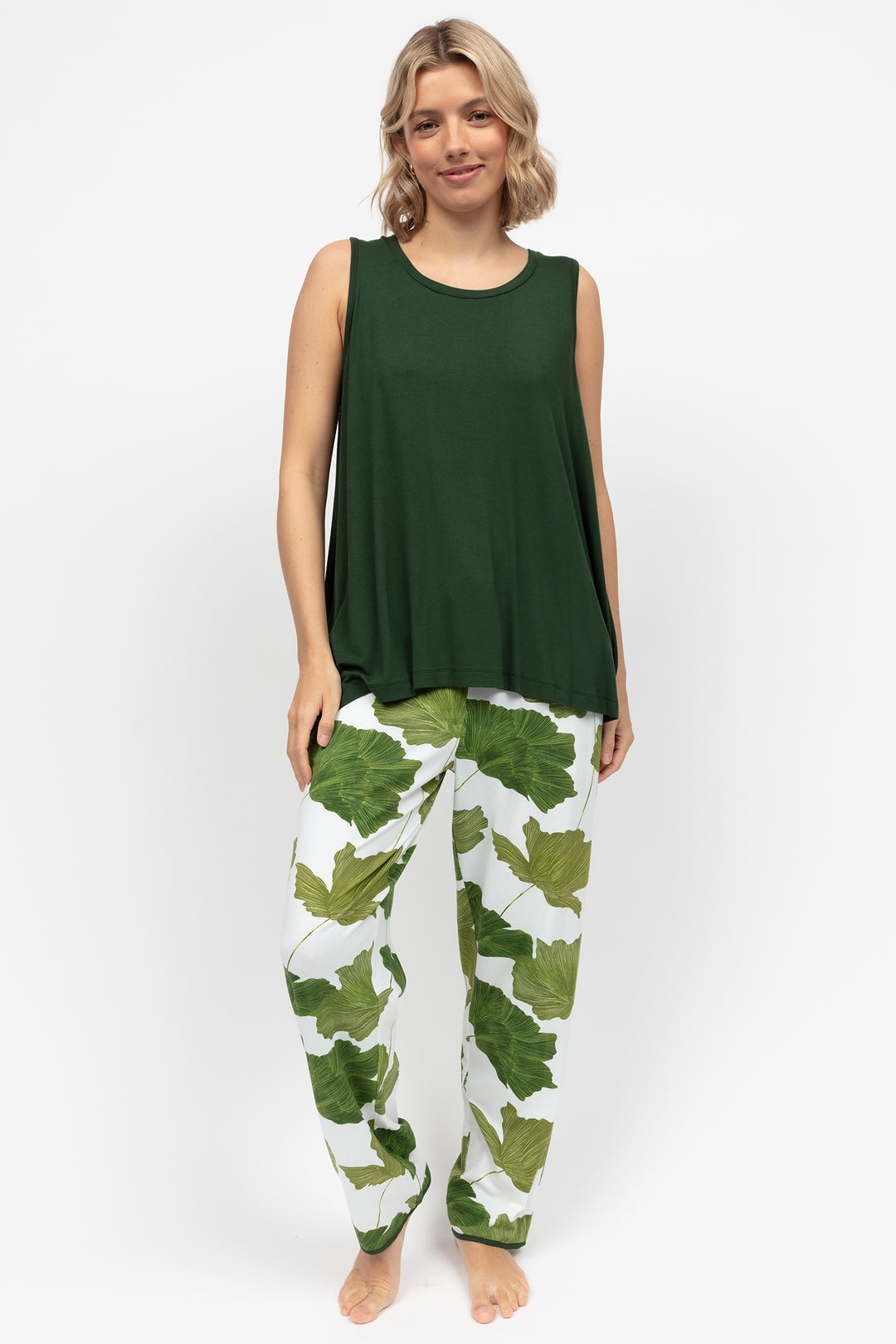 Woman wearing a green sleeveless top and leaf-patterned pants on a white background