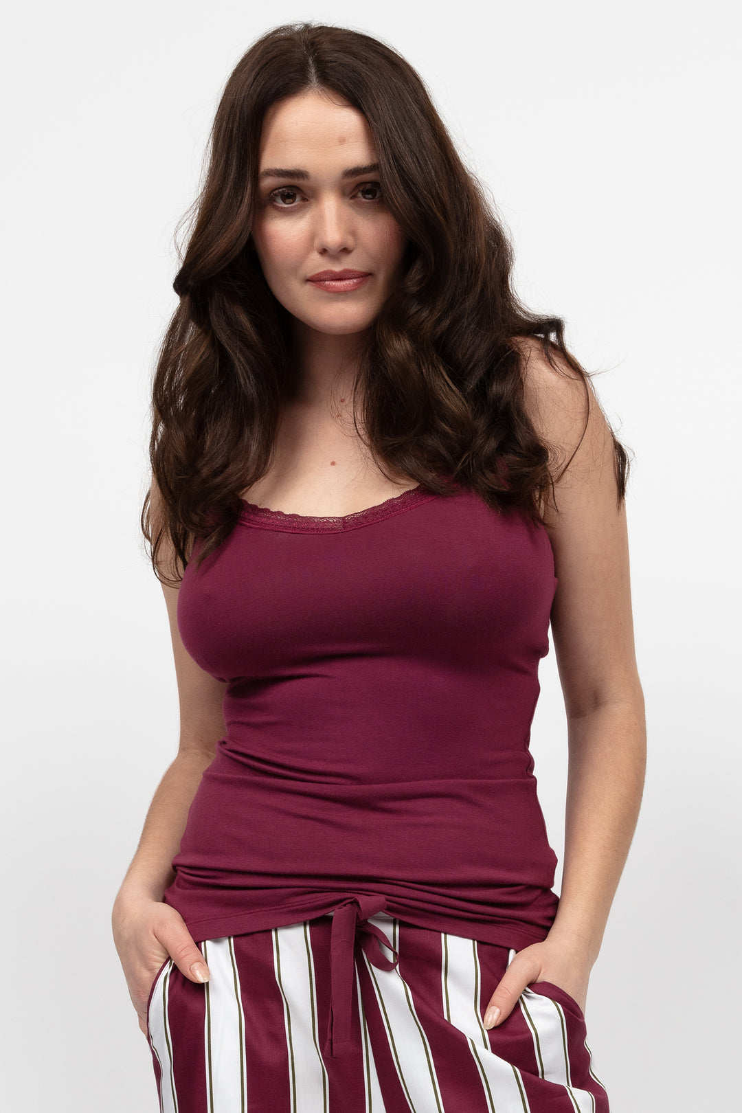 Woman wearing a maroon tank top and striped pants on a white background